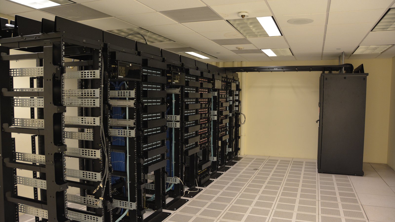 Rows of black server racks stand beneath cable trays inside a data center.