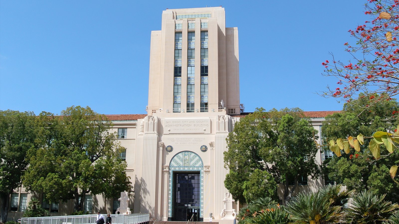 The pink-roofed San Diego County Administration Center stands beside the waterfront under a blue sky.