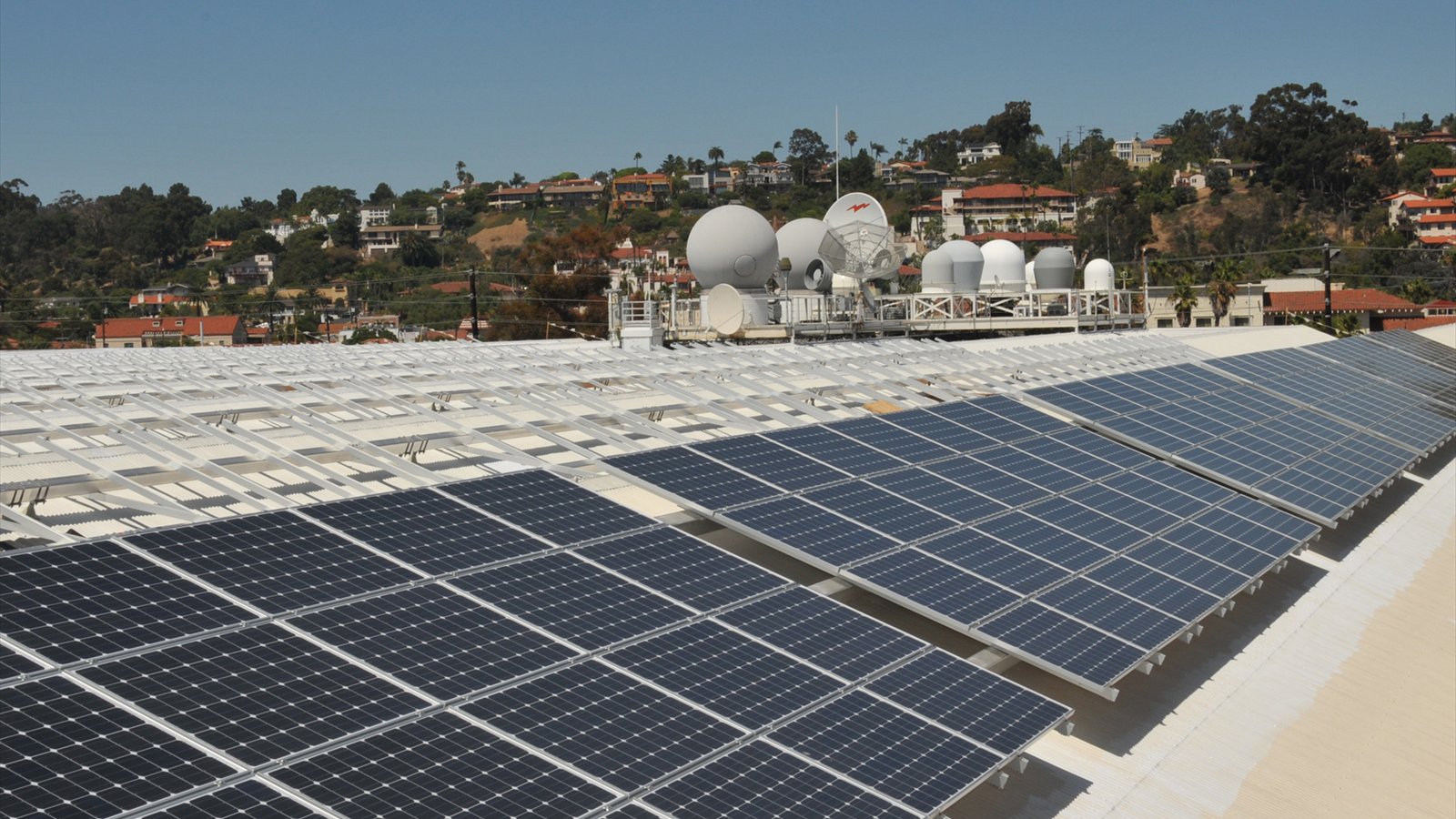 Rows of dark solar panels cover a broad rooftop above industrial buildings in San Diego's Old Town area.