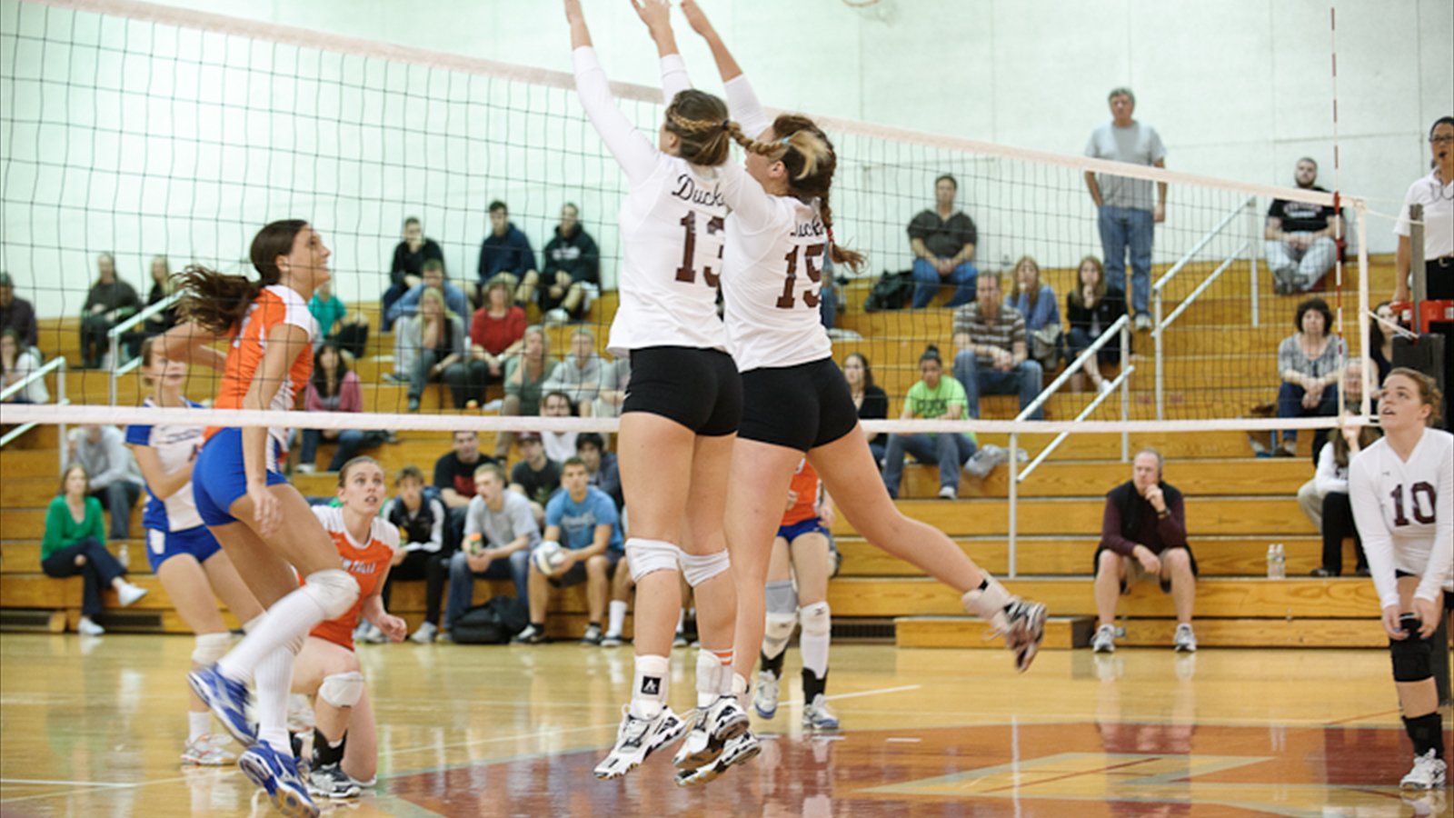 Women's college volleyball players prepare for the ball during an indoor match.