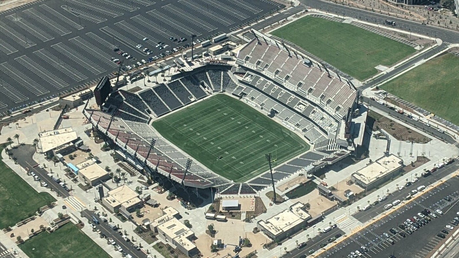 An aerial view looks into Snapdragon Stadium, showing a marked football field, grandstands and surrounding parking lots.