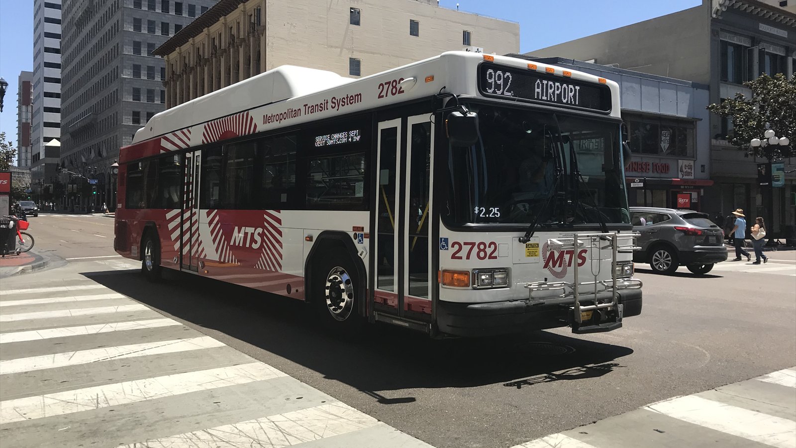 A San Diego MTS Route 992 bus marked for the airport traveling through a downtown intersection.