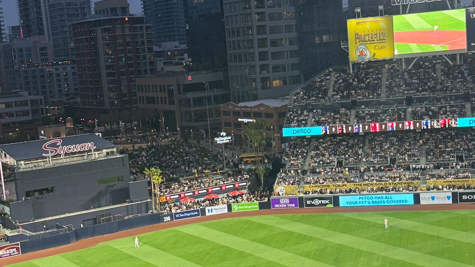 A baseball game at Petco Park viewed across the outfield toward the illuminated scoreboard and downtown towers.