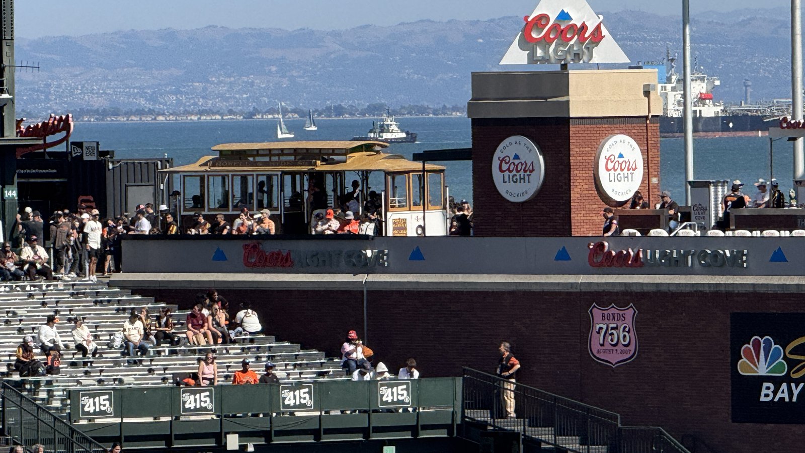 Fans sit and walk through the right-field seating and concourse at Oracle Park with San Francisco Bay behind them.