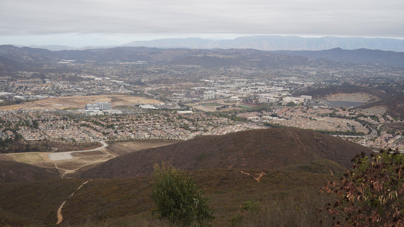Cal State San Marcos buildings and surrounding neighborhoods spread across rolling terrain beneath an overcast sky.