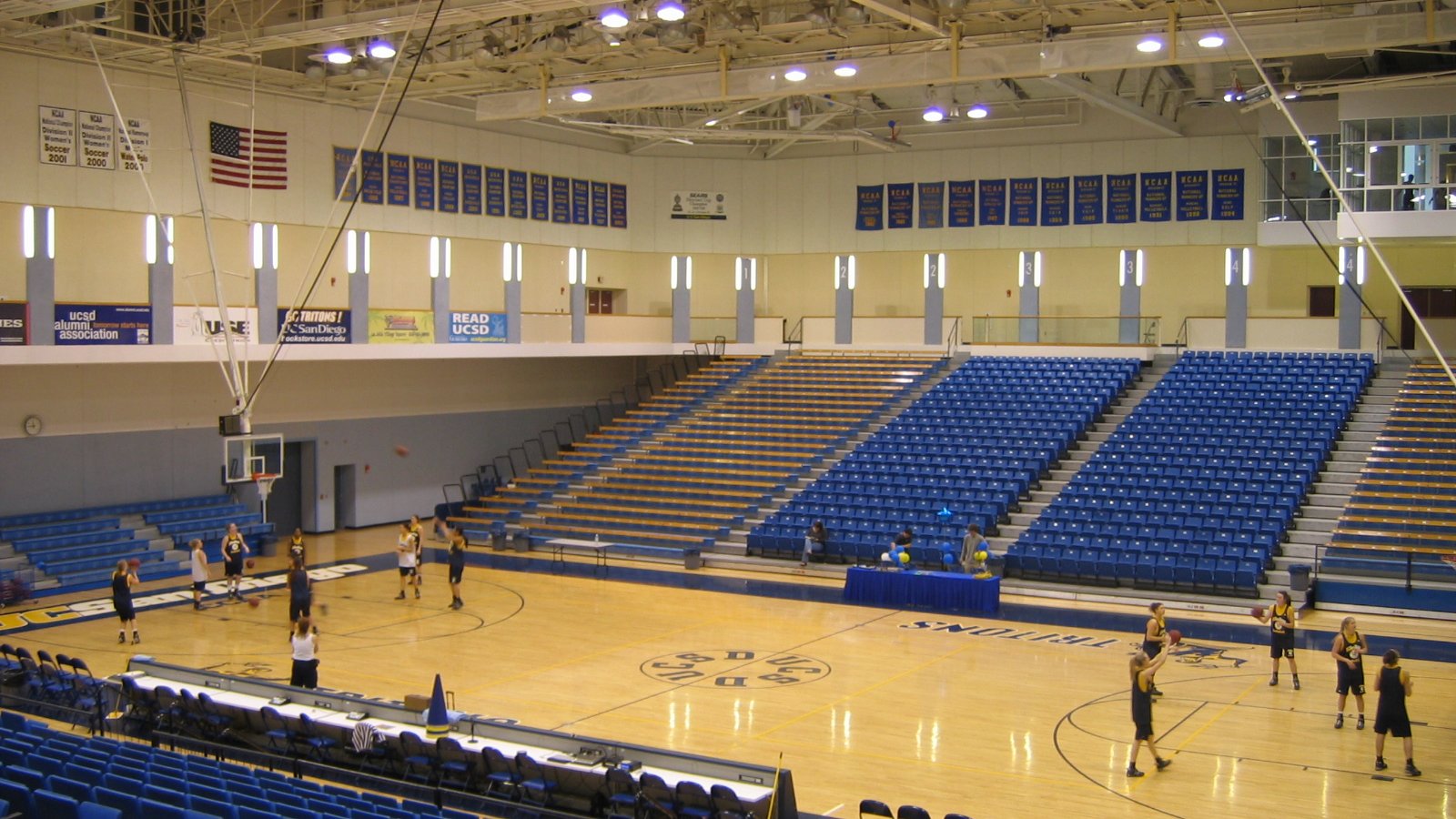 Blue retractable seats surround a basketball court inside a college arena.