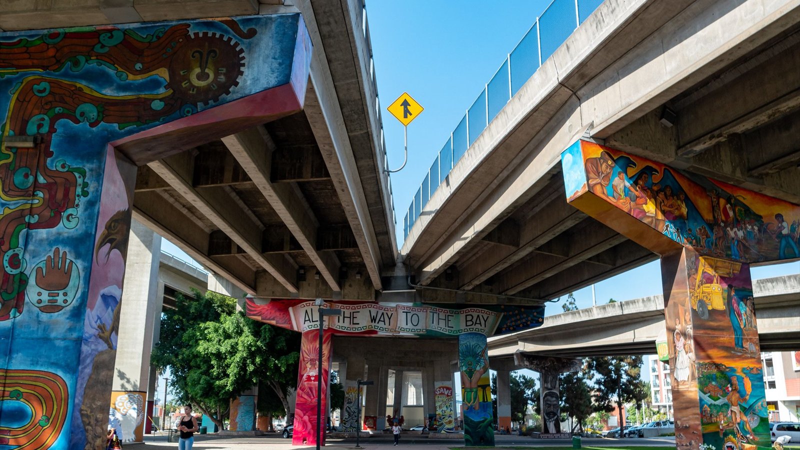 A colorful Chicano Park mural reads All the Way to the Bay beneath a freeway structure.