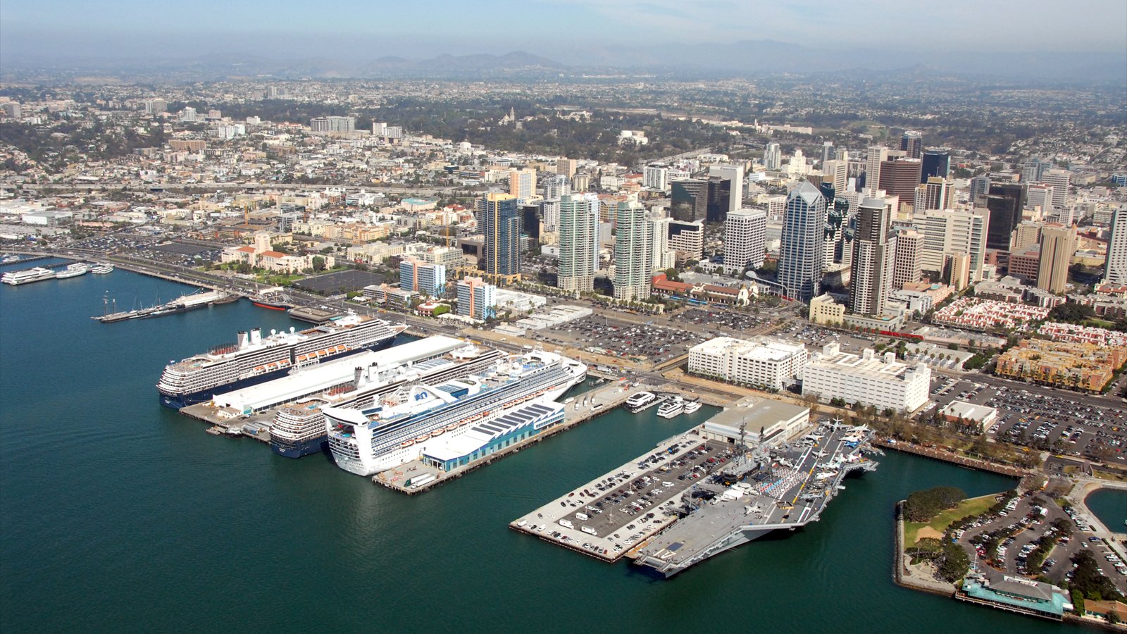 Three cruise ships line San Diego's waterfront near the white-roofed cruise terminals and USS Midway Museum.