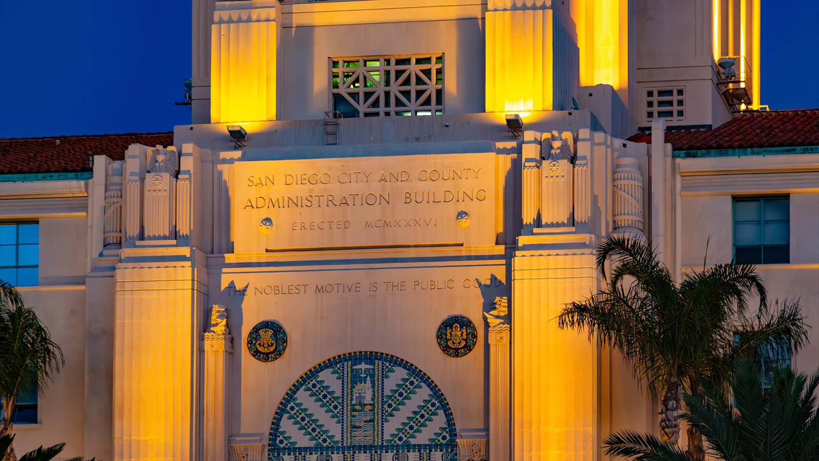 The illuminated facade of the San Diego City and County Administration Building fills the frame beneath a deep blue sky.
