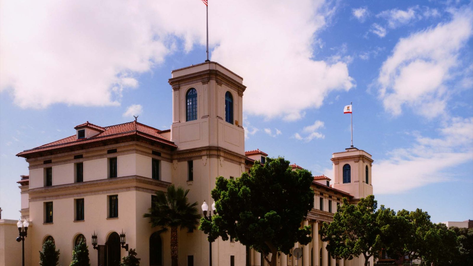 The cream-colored Jacob Weinberger U.S. Courthouse rises beneath a blue sky with red-tiled roofs and two square towers.