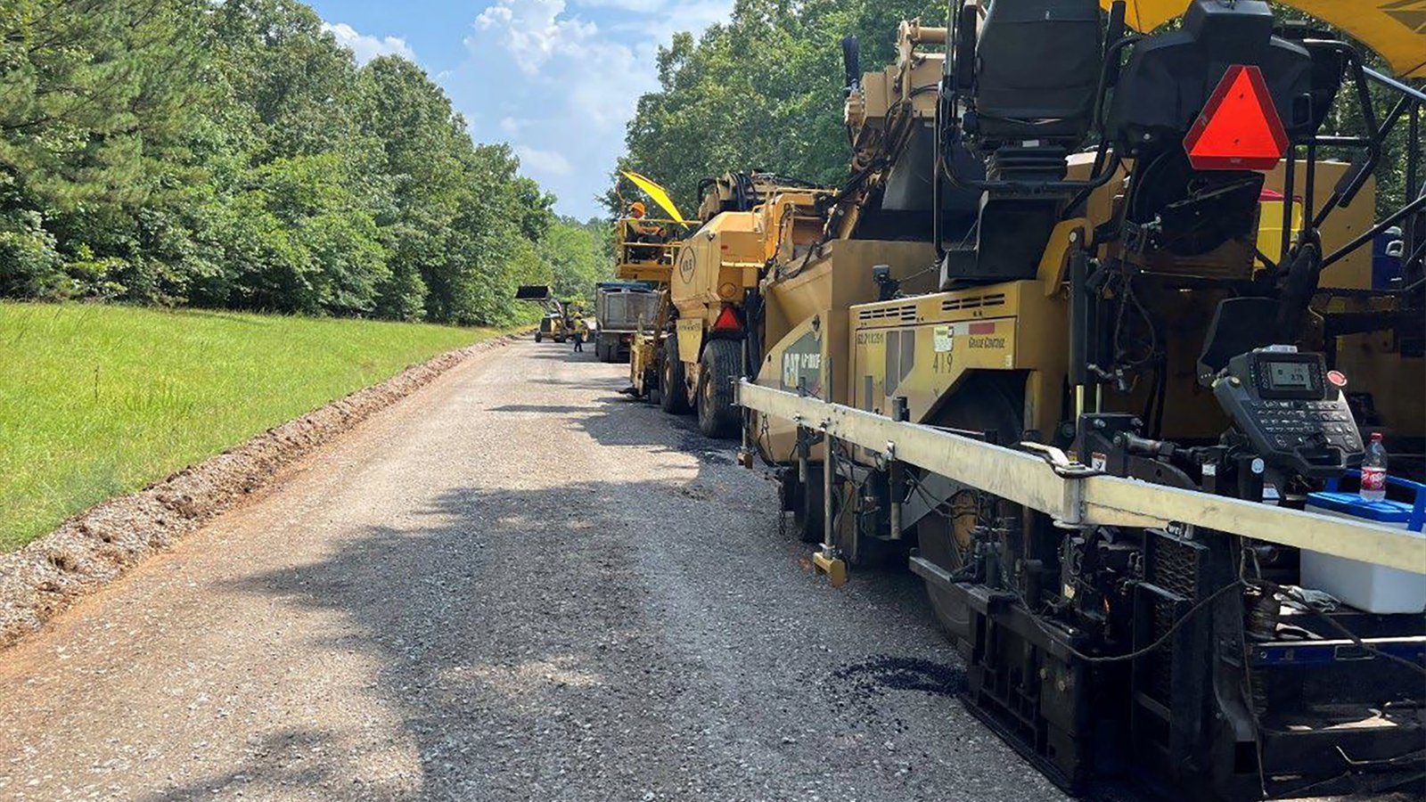 Dump trucks and tracked paving machines place asphalt along a scraped roadway.