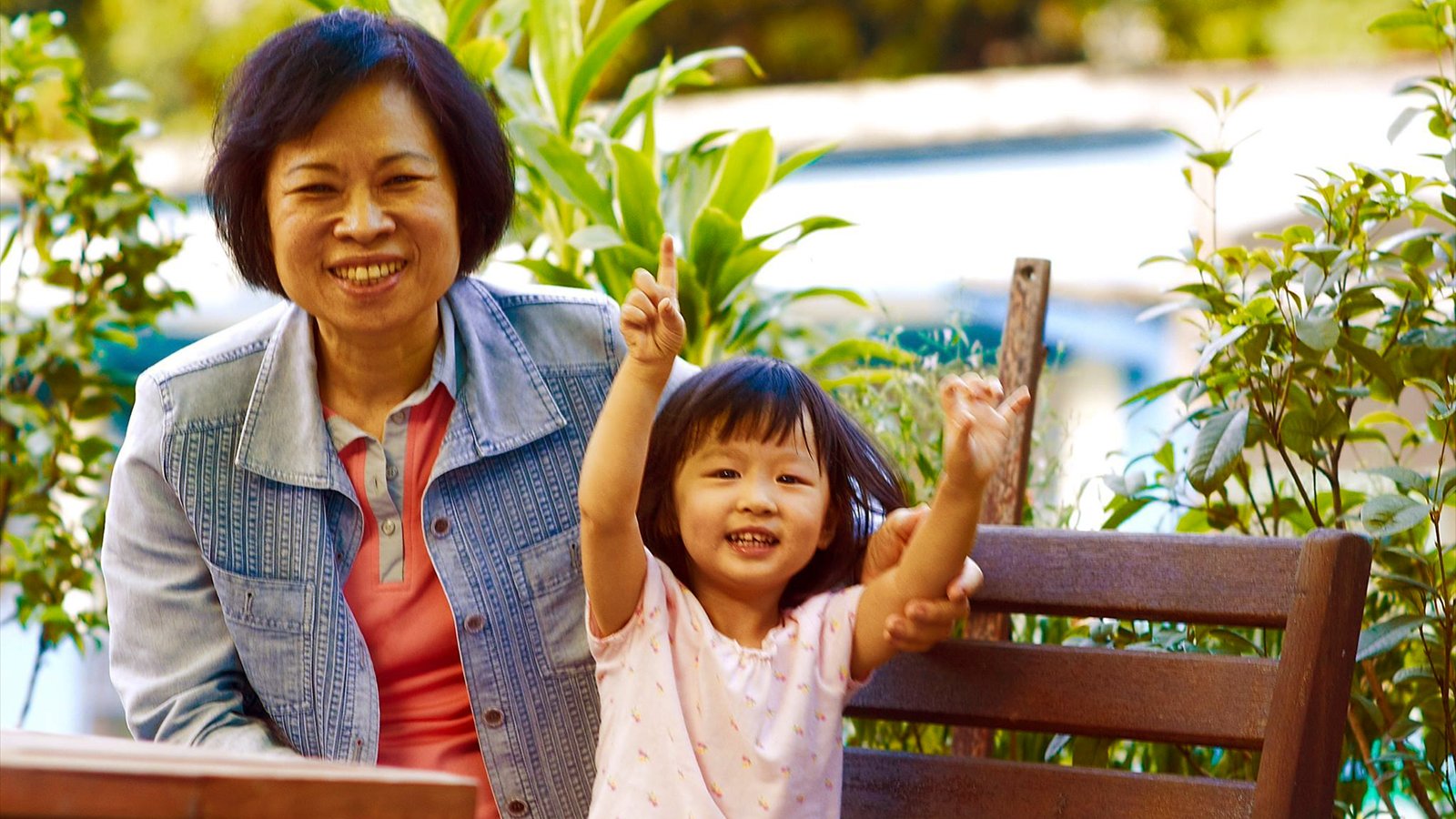 An older woman and a young girl stand close together and smile outdoors.
