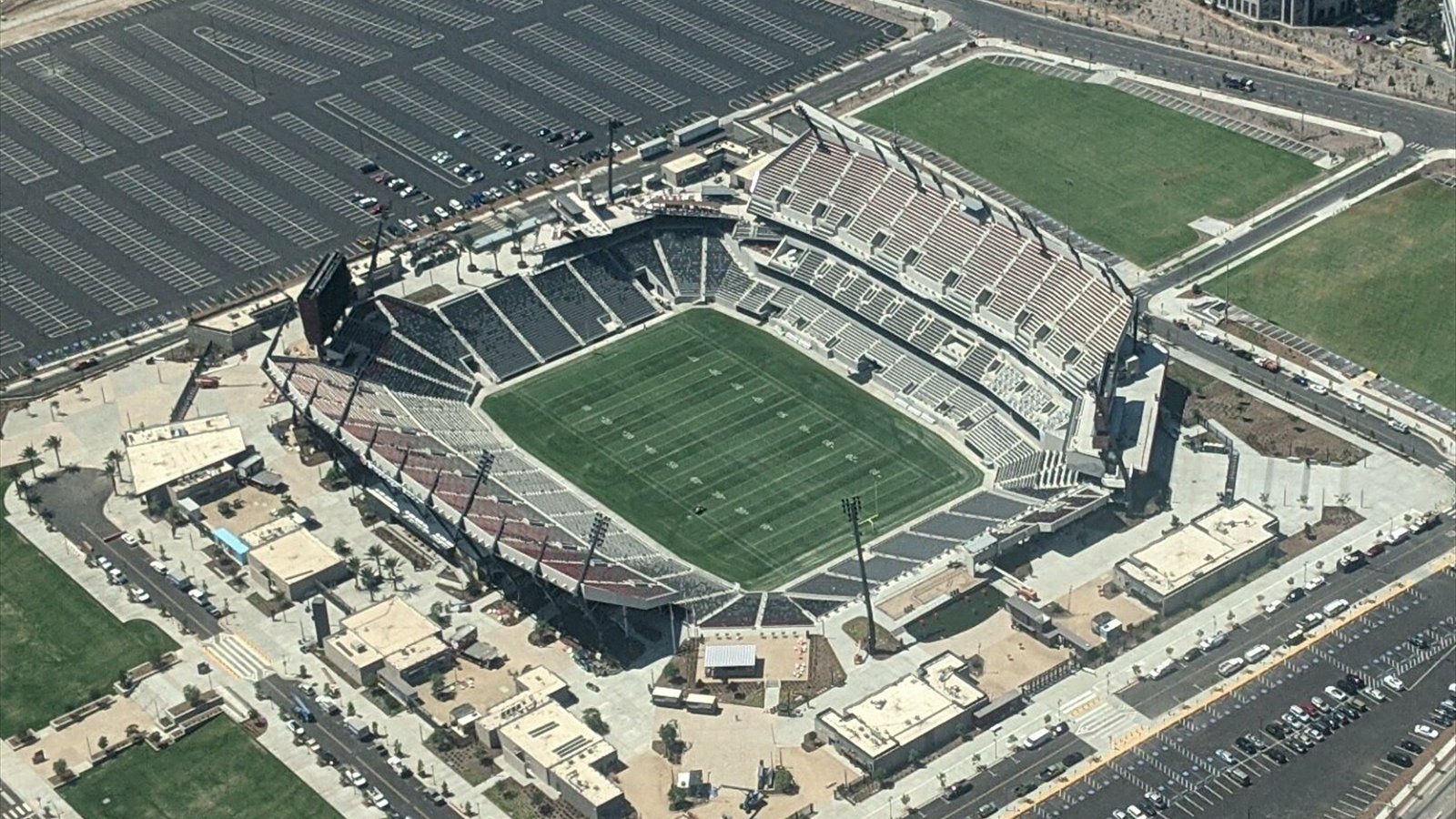 An aerial view looks down into Snapdragon Stadium, its marked football field, steep grandstands and surrounding parking lots.