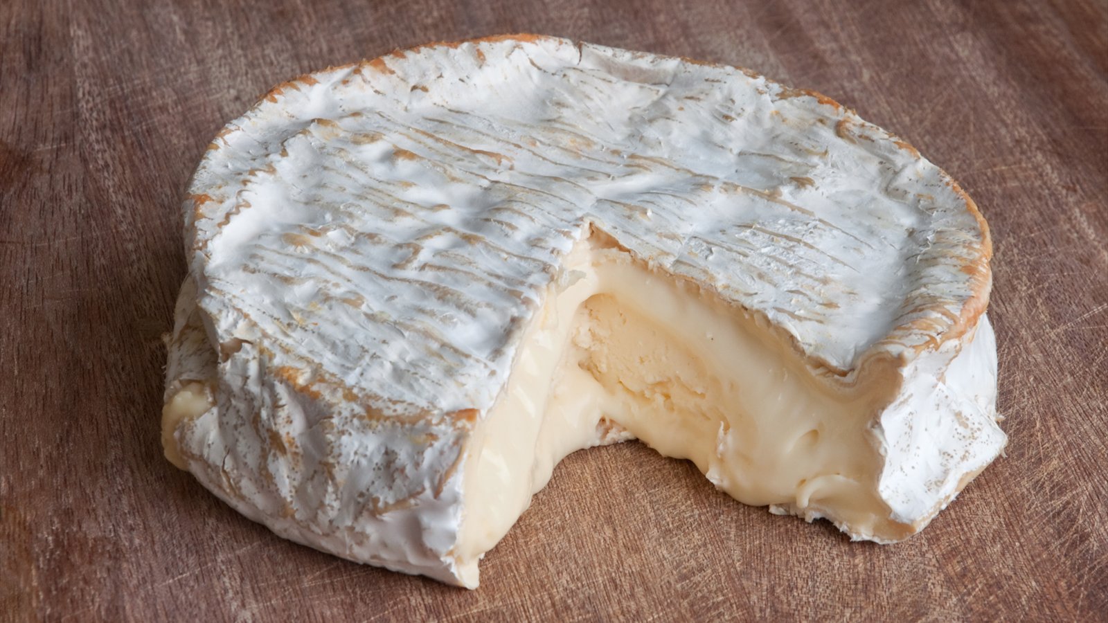A round wheel of unpasteurized cow's-milk cheese rests on a wooden board.