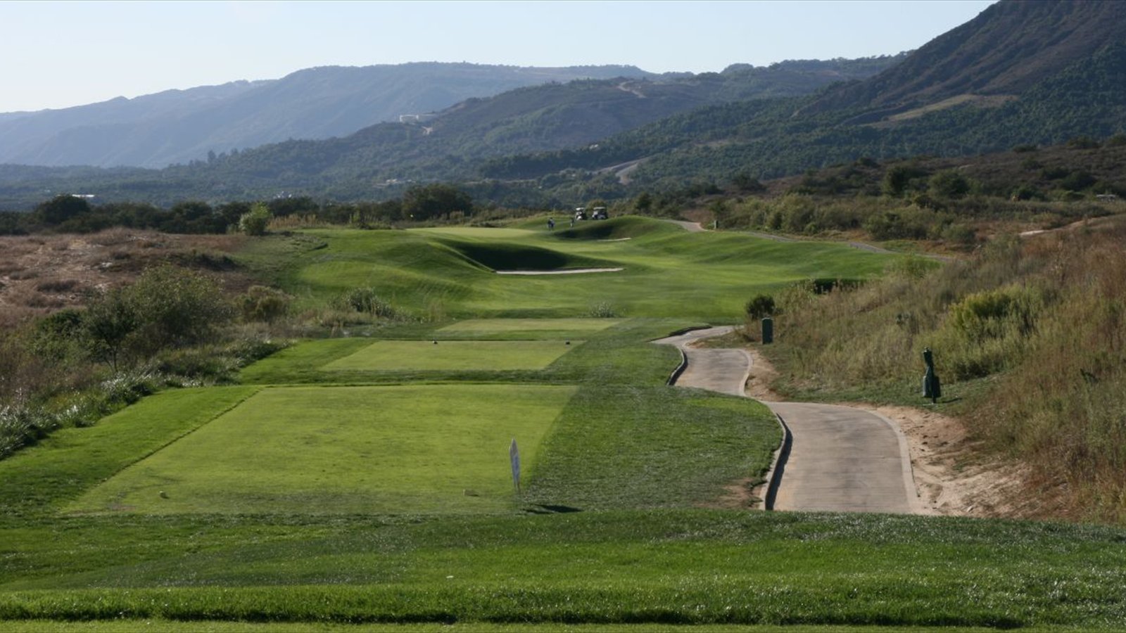 A golf fairway curves past a bunker and cart path beneath rugged hills in Rancho Santa Fe.