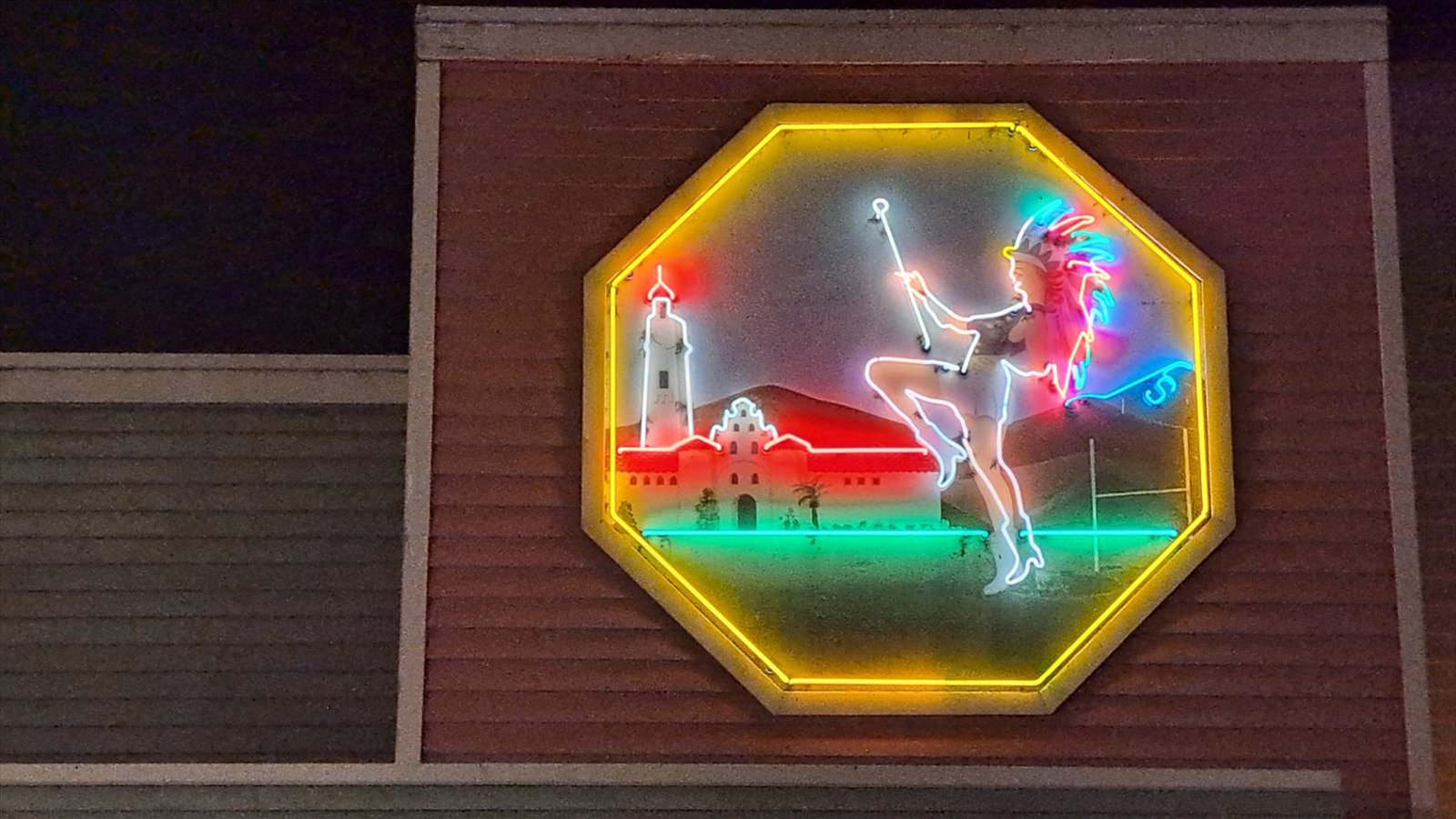Neon sign depicting a cheerleader in a non-Aztec native american headress standing at the corner of El Cajon Boulevard and College Avenue near San Diego State University, whose sports mascot is the Aztecs