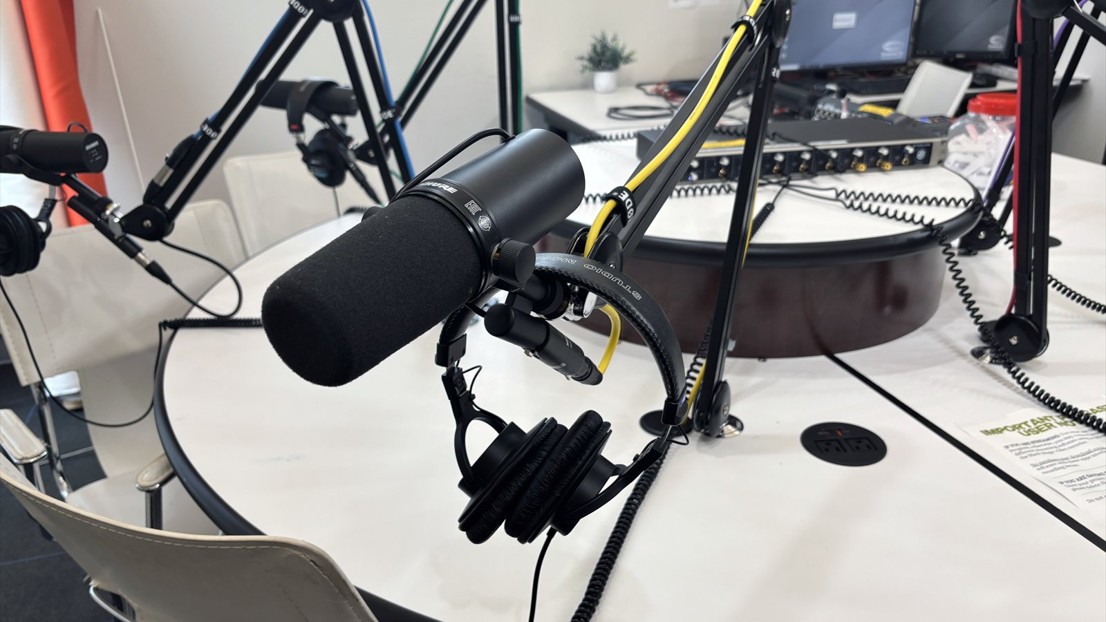 Black broadcast microphones and headphones hang from articulated arms around a round white table in a podcast studio.