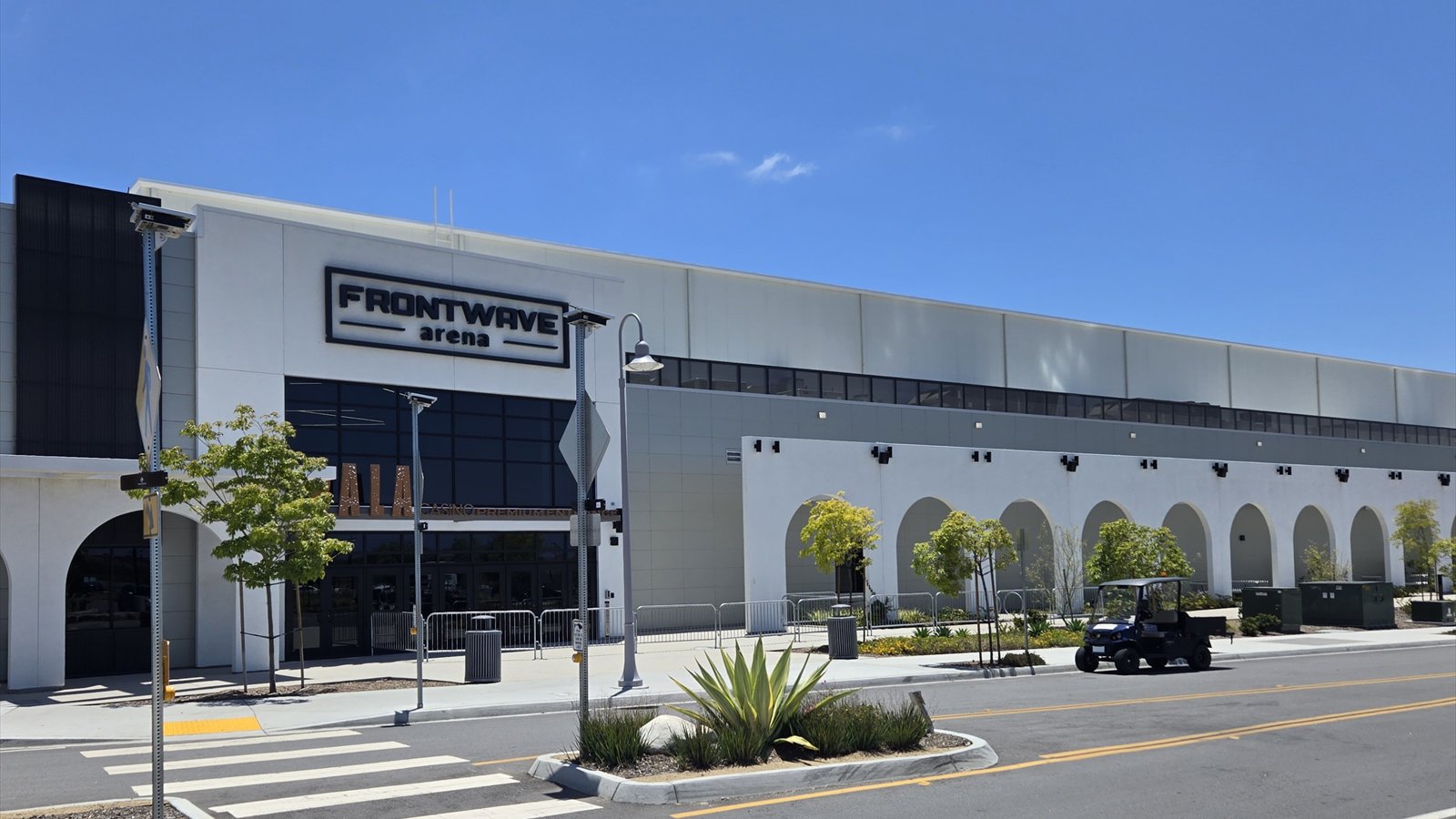 The angular gray exterior and covered premium entrance of Frontwave Arena stand beneath a blue sky.