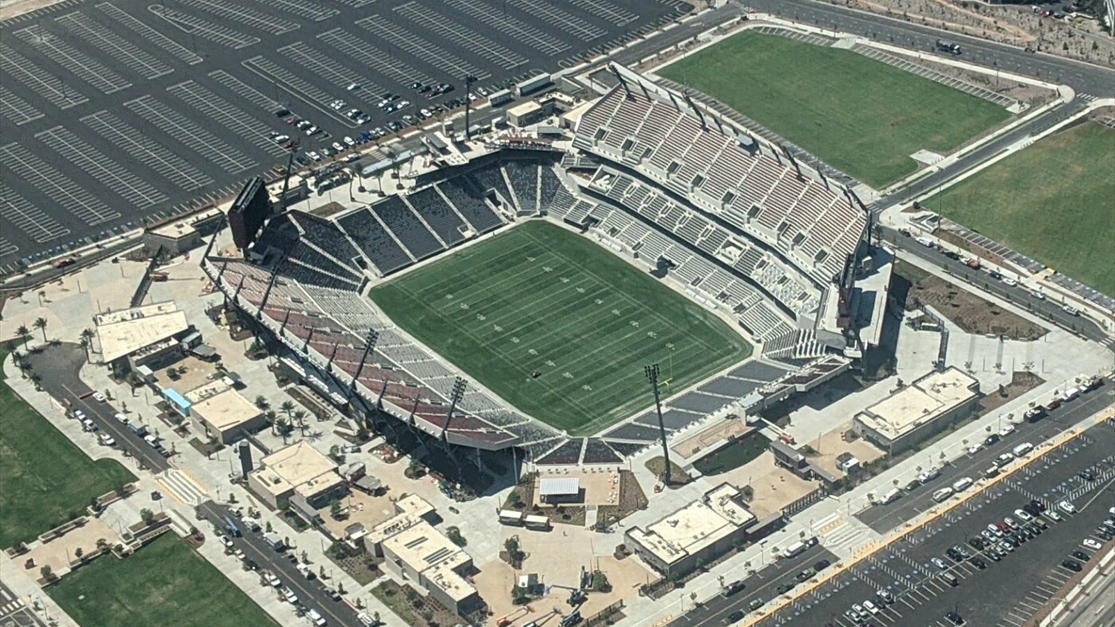 An aerial view looks down into Snapdragon Stadium, its marked football field, steep grandstands and surrounding parking lots.