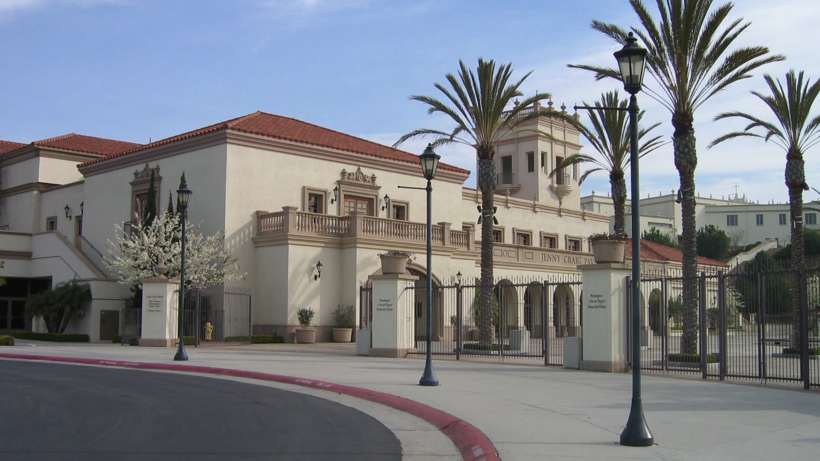 The tan exterior of Jenny Craig Pavilion stands behind palm trees on the University of San Diego campus.