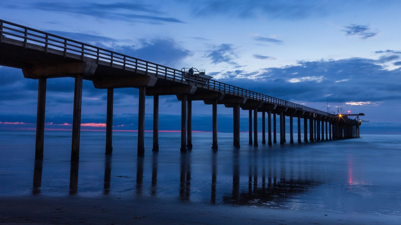 Scripps Pier extends across reflective ocean water beneath a cloudy blue twilight sky with a narrow pink horizon.