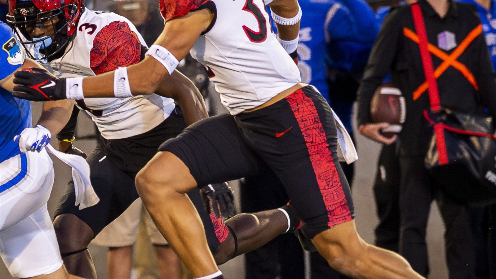 San Diego State football players in red helmets and white uniforms stand near the sideline during a game.