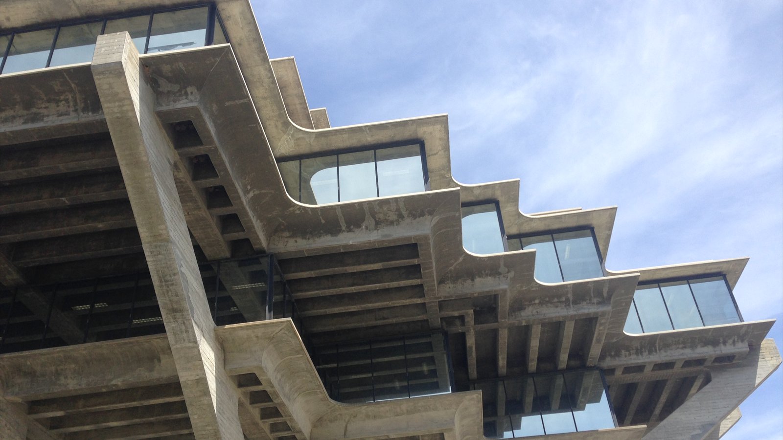The concrete cantilevers and dark windows of Geisel Library rise against a blue sky on the UC San Diego campus.