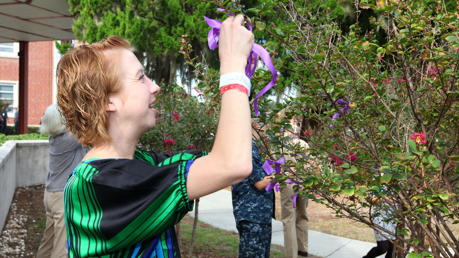A uniformed Marine ties a purple ribbon around a tree trunk during a domestic-abuse-awareness event.