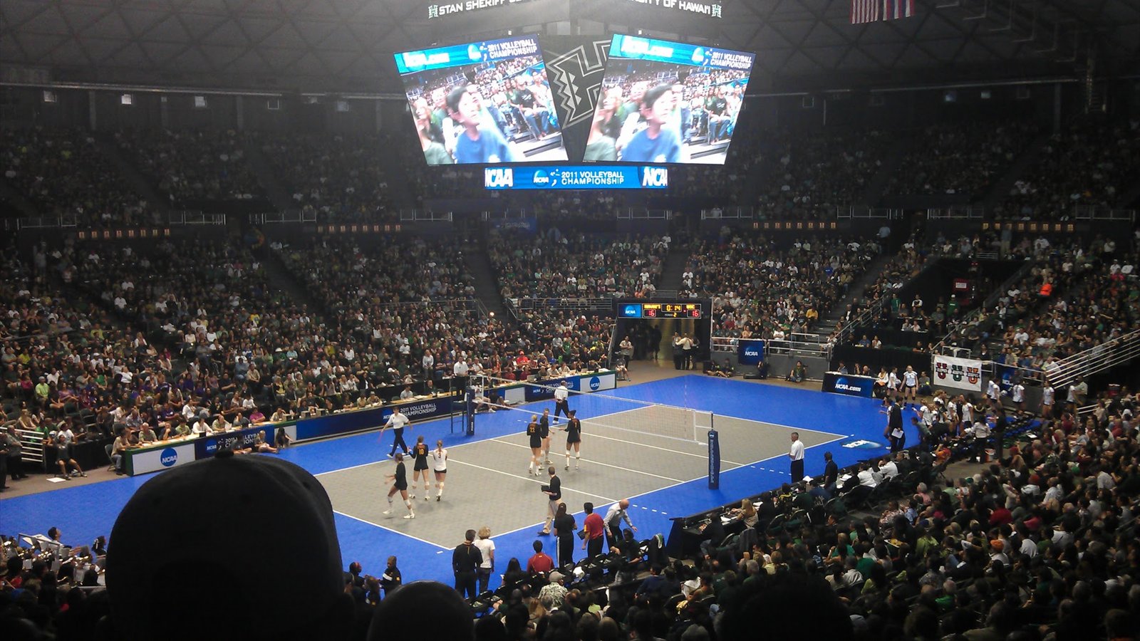 A volleyball court sits beneath a center-hung scoreboard in a packed Stan Sheriff Center in Honolulu.