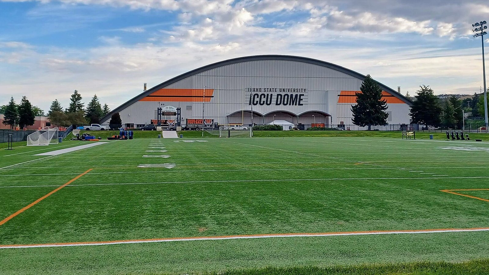A green football practice field stretches toward the arched exterior of Idaho State University's ICCU Dome.