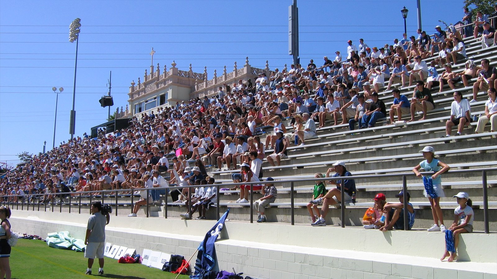 Crowded concrete grandstands rise beside the sunlit grass at Torero Stadium, with an ornate press box behind spectators.